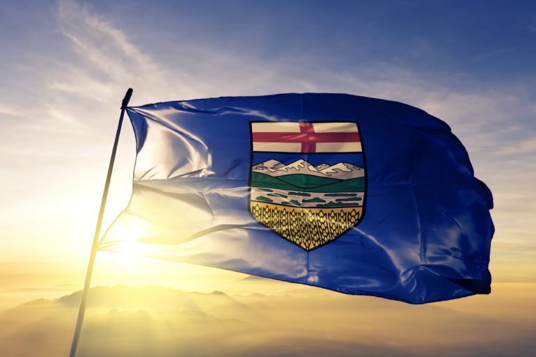 Alberta flag in front of the sun setting over the mountains.