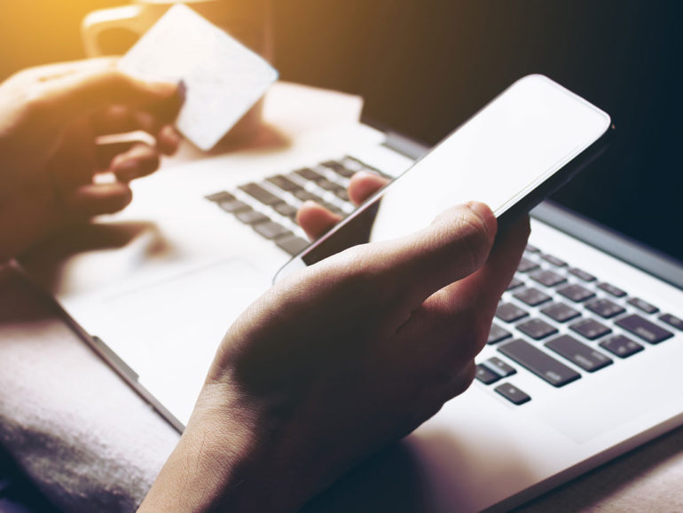 Close up of person looking at bank card, using mobile phone and laptop
